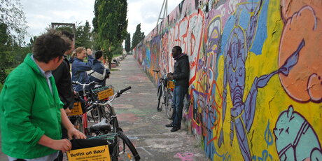 Guide mit Radgruppe vor GraffitiMauer
