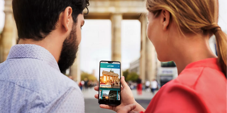 Junge Frau und junger Mann mit Blick auf ihr Handy mit der visitBerlin app ABOUT BERLIN. Im Hintergrund das Brandenburger Tor in Berlin.