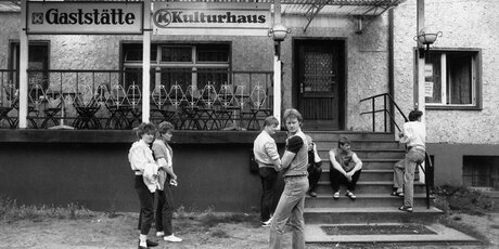 Schwarz-Weiß-Fo­to, Jugentliche in der DDR vor dem Eigang eines Kulturhauses