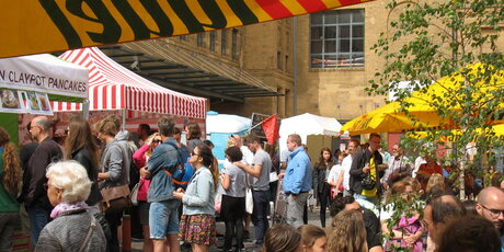 Besucher vor Ständen und an Tischen auf dem Street Food Markt