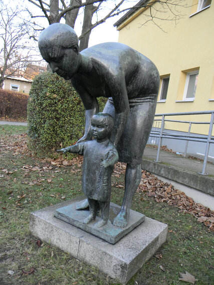 Standort: Pieskower Weg 48, Vorgarten der Kita "Sonnenblume", "Mutter mit Kind", Künstlerin: Lore Plietzsch (*1930), Datierung: 1964, Material: Bronze