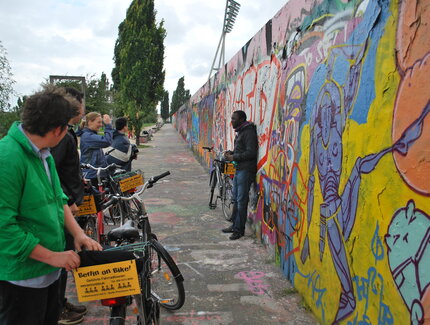 Guide mit Radgruppe vor GraffitiMauer