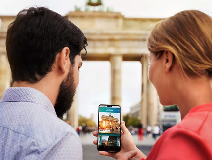 Junge Frau und junger Mann mit Blick auf ihr Handy mit der visitBerlin app ABOUT BERLIN. Im Hintergrund das Brandenburger Tor in Berlin.