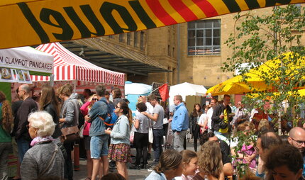 Besucher vor Ständen und an Tischen auf dem Street Food Markt